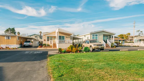 Three mobile homes rest beyond a small field of grass on a sunny day.