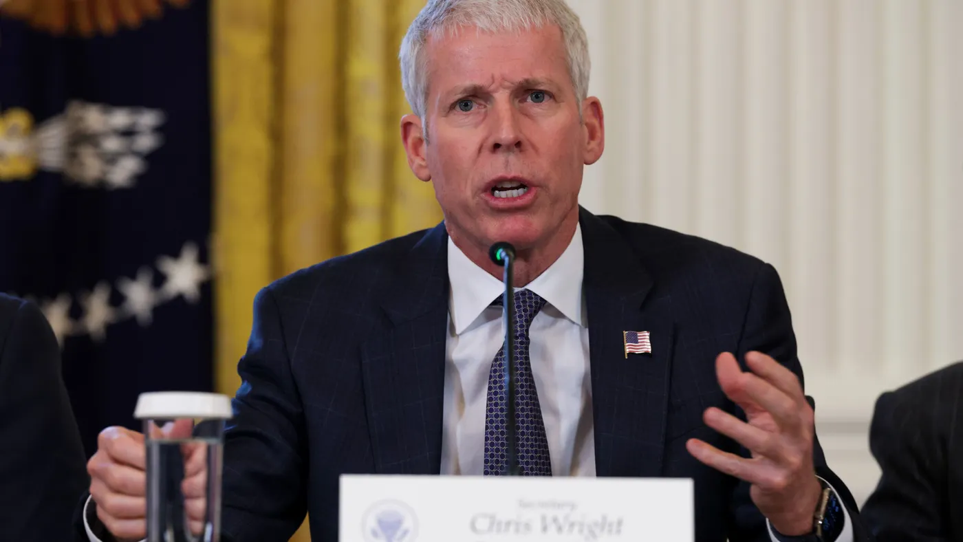 A man speaks at a microphone in from of a name sign that says Chris Wright, Department of Energy.