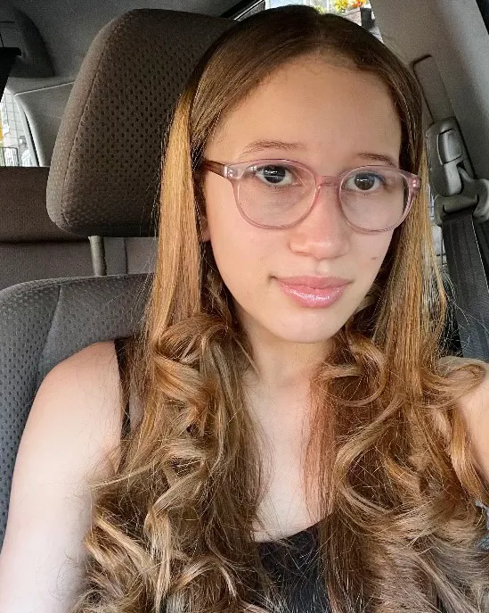 A student sits in a car looking at the camera