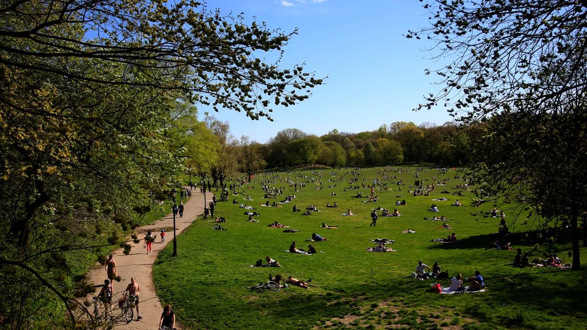 People in a park on a sunny day. Cyclists and pedestrians walk on a path next to a grassy area.