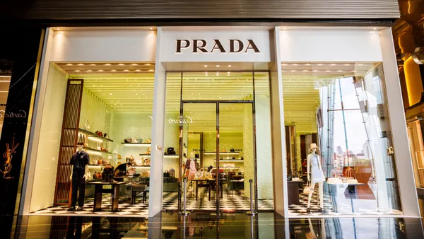 A storefront with the word Prada written on the front is lit up within.