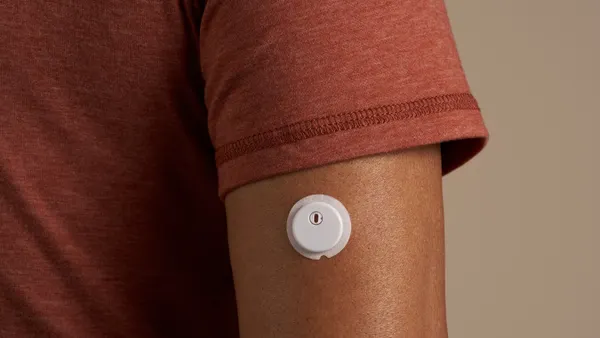 A white, round device is stuck on a person's arm below their sleeve.