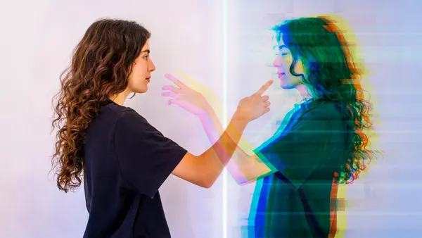A young woman faces her digital twin, reaching out to make contact.
