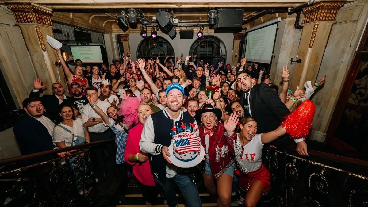 An image of a group of people with a person in the front holding a cake with an American flag on it wiht the words TGI Fridays