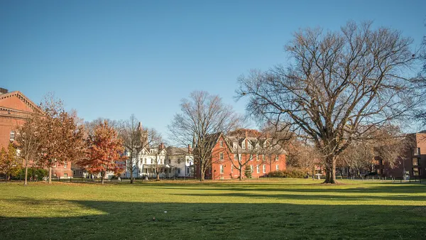 A green lawn in the fore- and mid-ground, and a series of brick, academic-looking buildings in the farground.