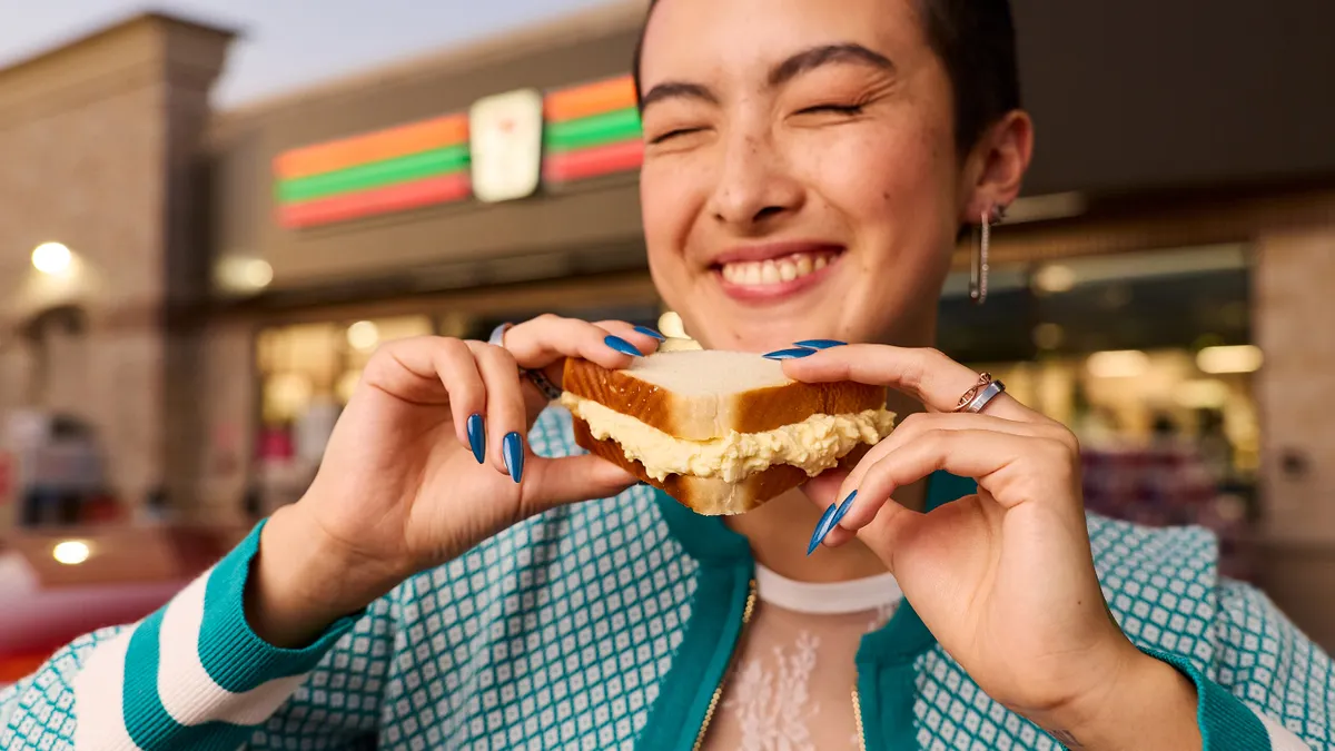 A photo of aperson holding an egg sandwich outside of a store. A Sign above the door on the store says 7-Eleven.