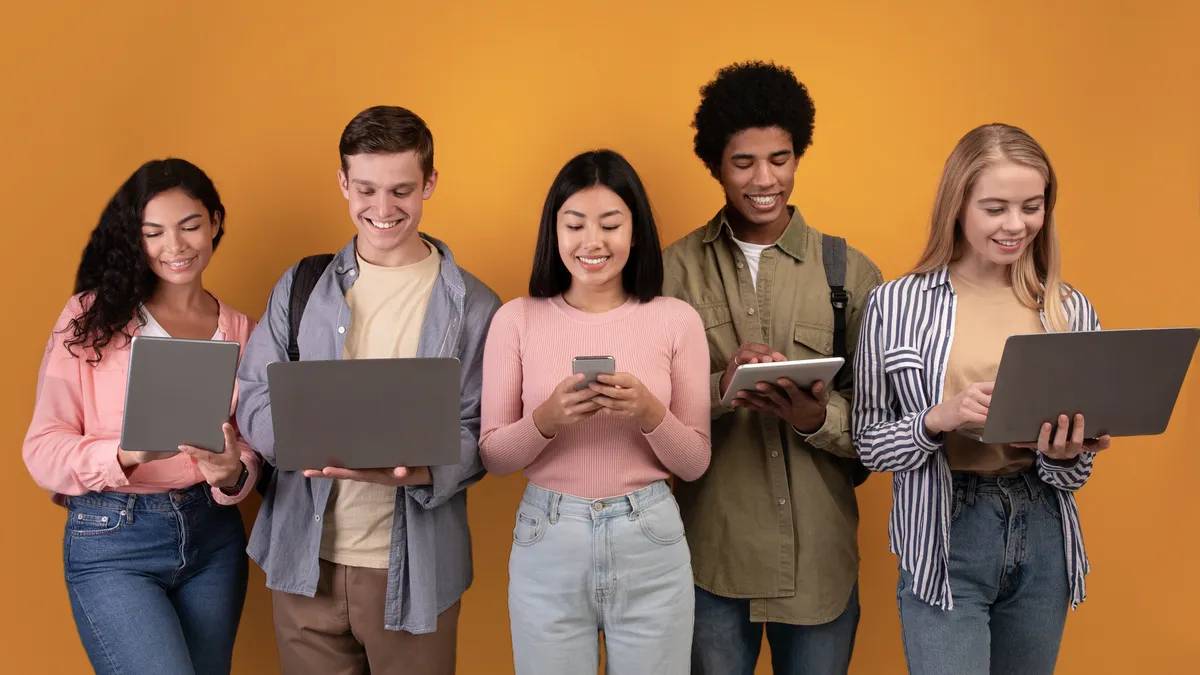 A group of young people on computers, phones and tablets.