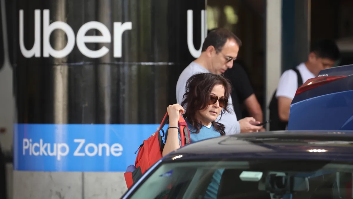 People line up for their rides in front of a sign that reads "Uber Pickup Zone."