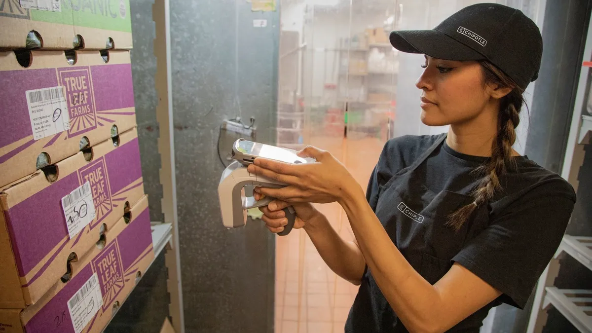 A restaurant employee using RFID to scan a box with a barcode.