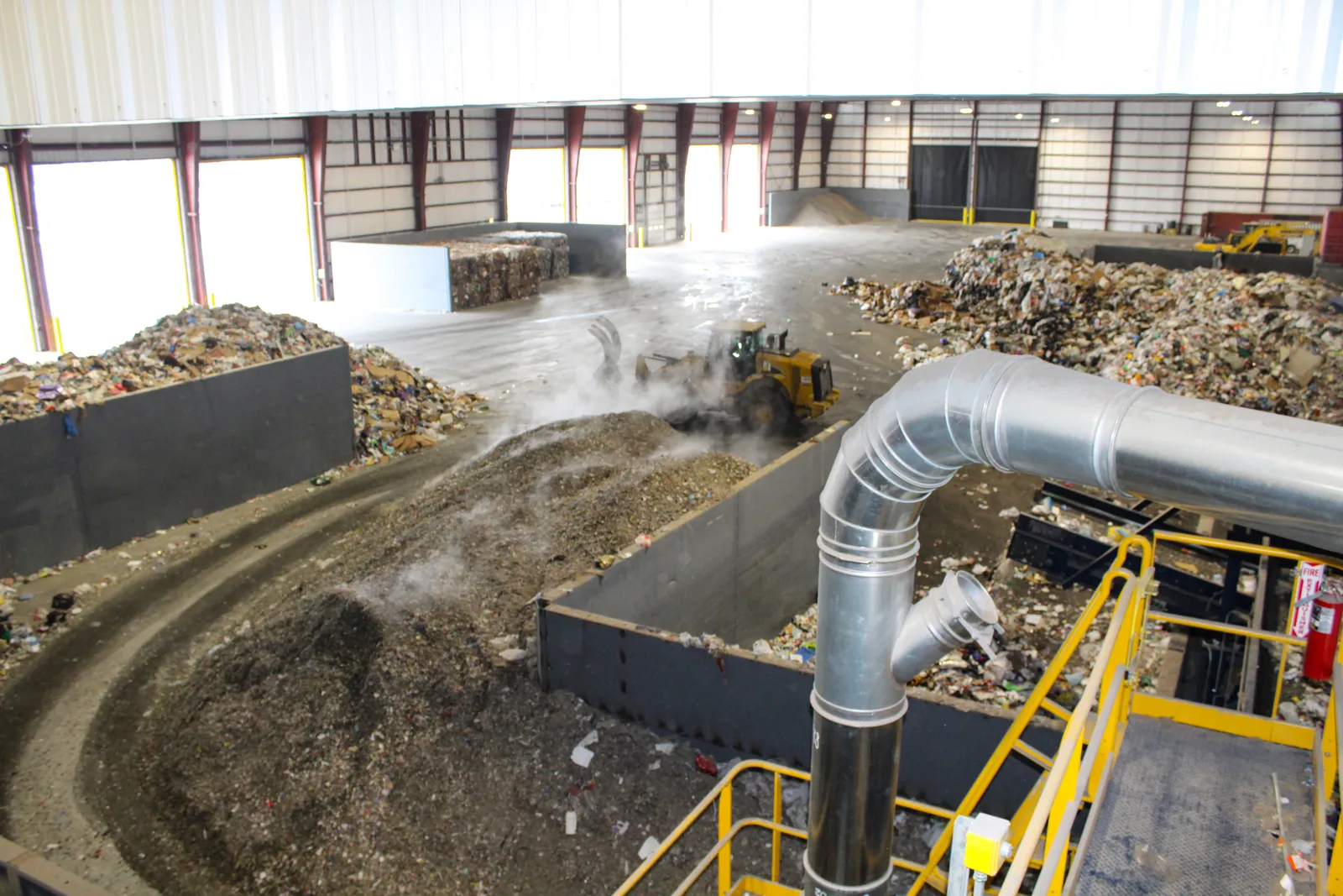 A front enloader moves recyclables into piles in a warehouse where material is stored.