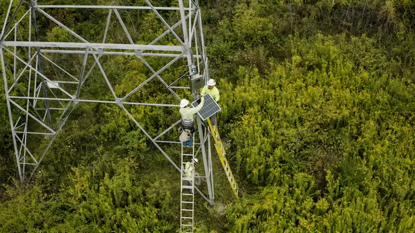 Workers installing dynamic line rating equipment on a transmission tower.