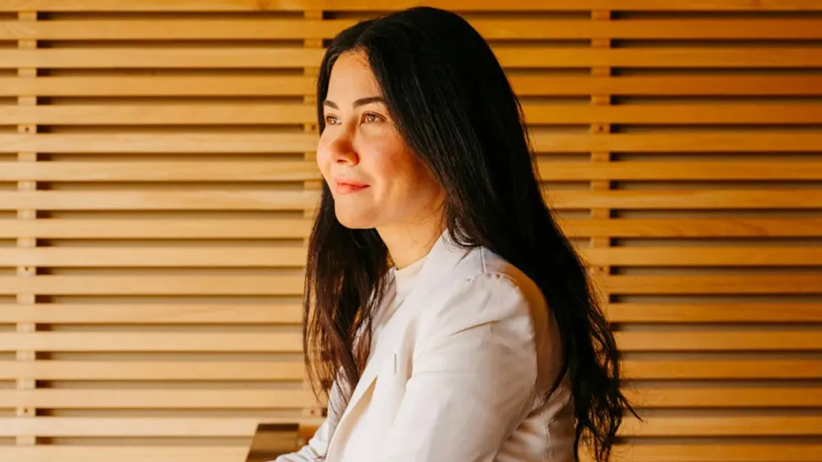 A woman in a white blazer looking to the left while leaning on a wooden railing