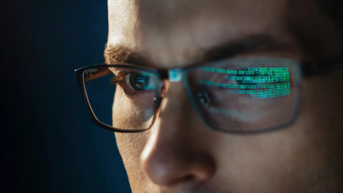 Close-up of person wearing glasses looking at a computer screen and HTML blockchain reflected in glasses.