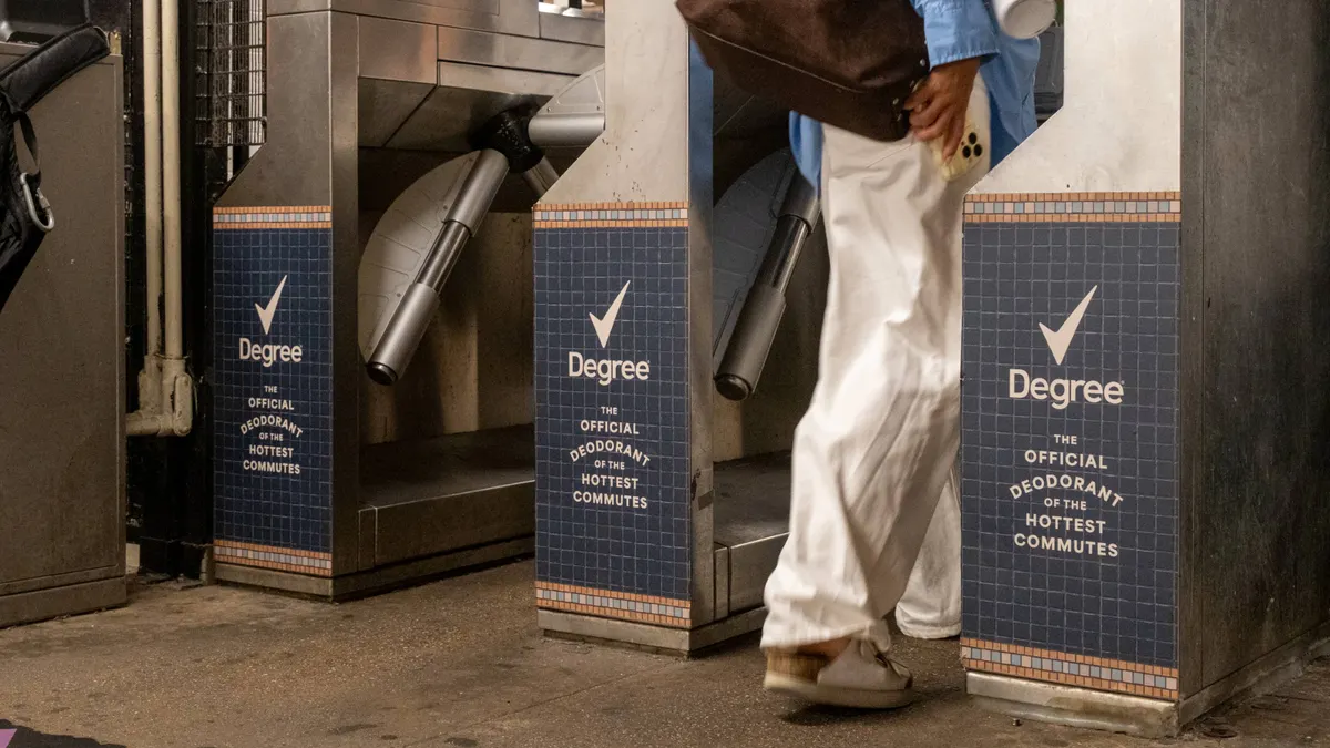 Commuters pass through a row of New York City subway turnstiles that feature ads from Degree.