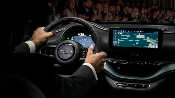 A driver hands are visible sitting behind the wheel of a 2025 Fiat 500e electric car.