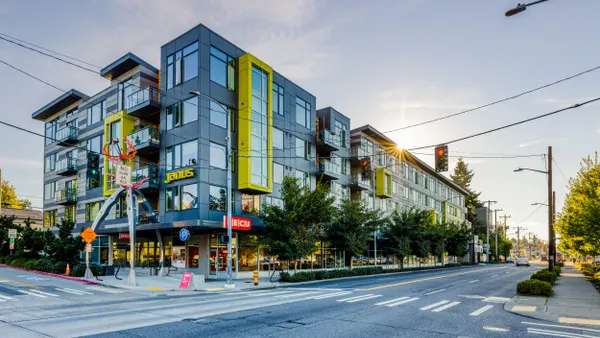 Grey and yellow, five-story apartments with ground floor retail on street corner.