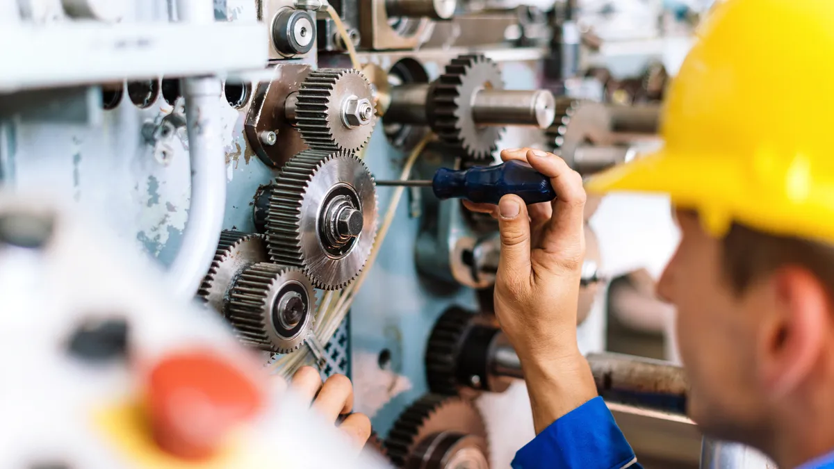 A worker performs maintenance on a machine in a factory.