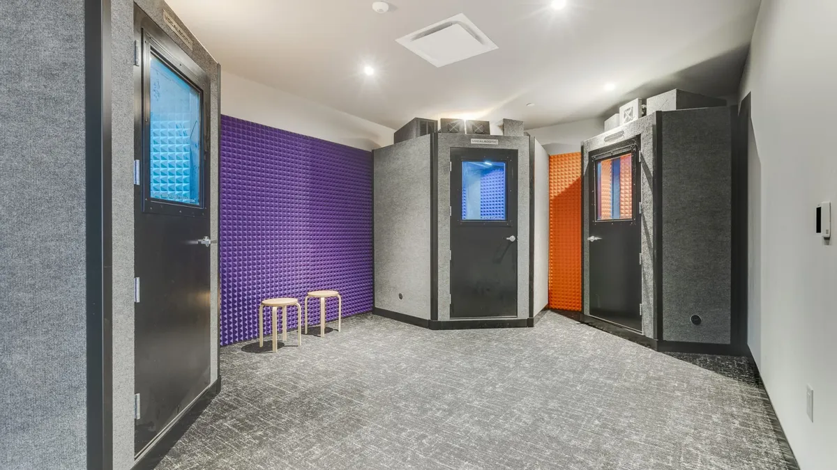 A small room with purple soundproofing foam on the walls and three soundproof pods.