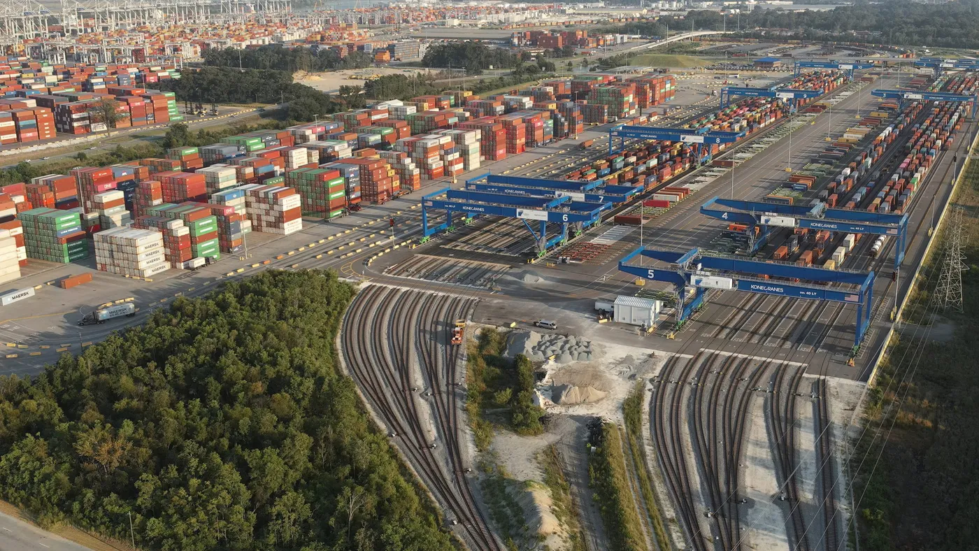 An aerial view of  shipping containers and rail trackers behind a shipping port.