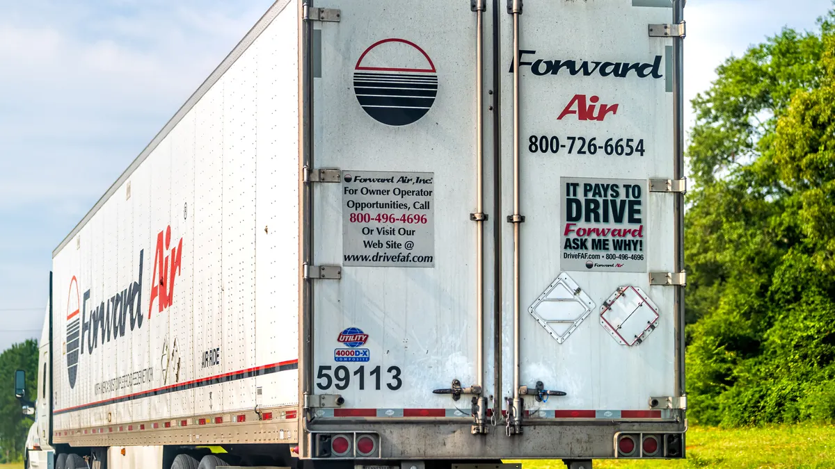 A Forward Air refrigerated trailer on the road with trees and shrubs in the background.