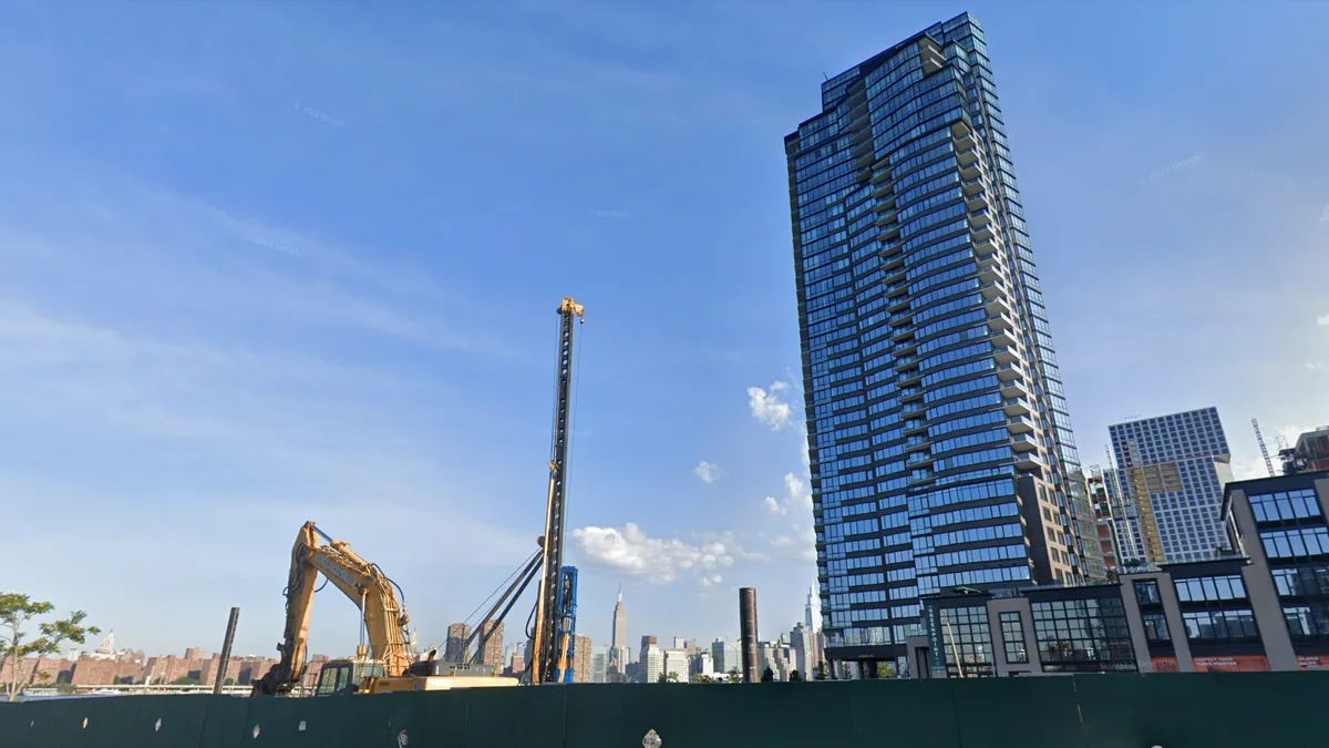 An excavator digs next to a larger tower.