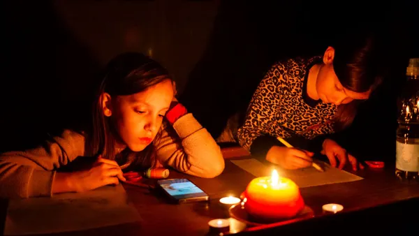 Two little girls draw on a table with a candle during a power outage