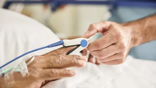 A person places a pulse oximeter clip on another person's finger.