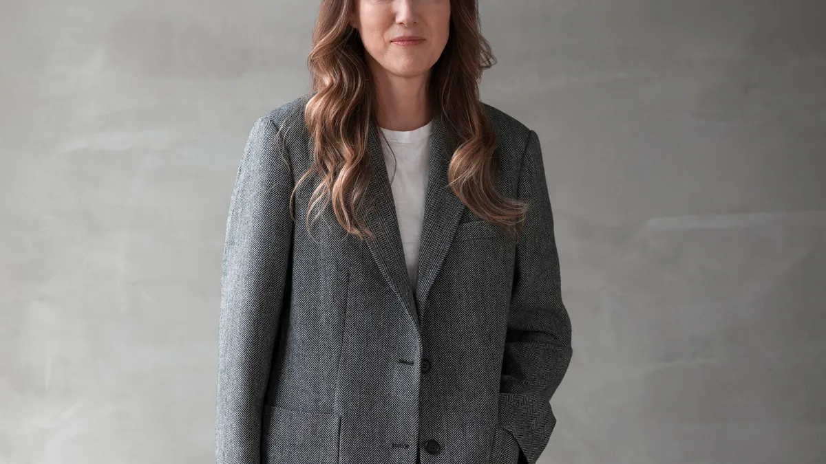 Clare Waight Keller stands for a professional headshot wearing an oversized suit set.