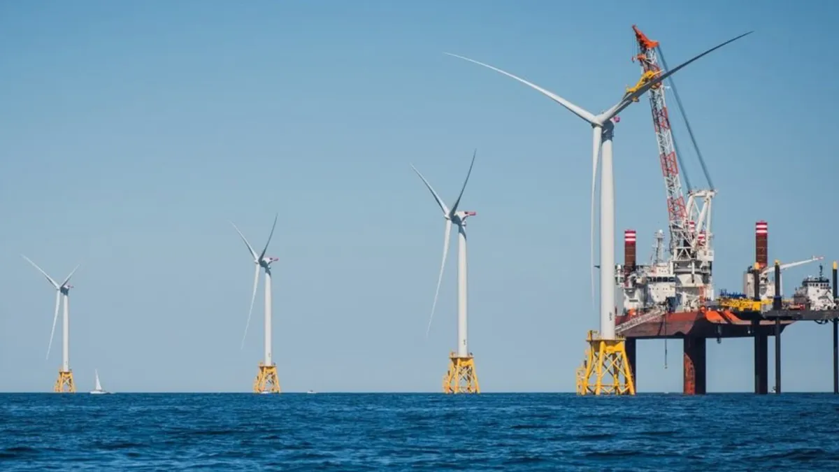 WInd turbines stand in dark blue water.