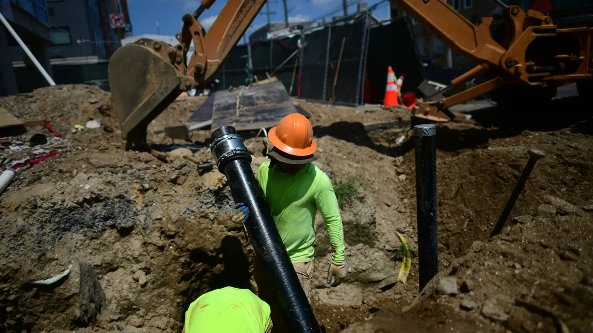 Two construction workers bend over in a trench installing a large pipe.