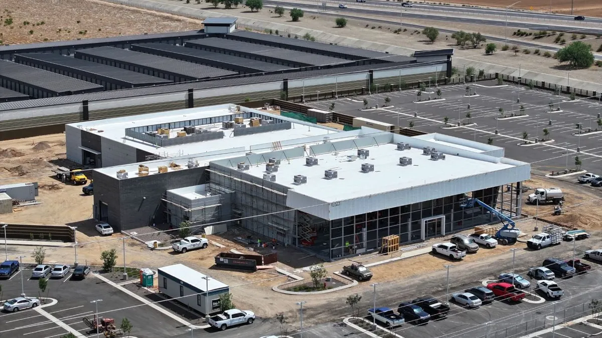 An aerial view of a building on a desert-like type of ground, with cars in a parking lot surrounding the sleek and shiny structure.