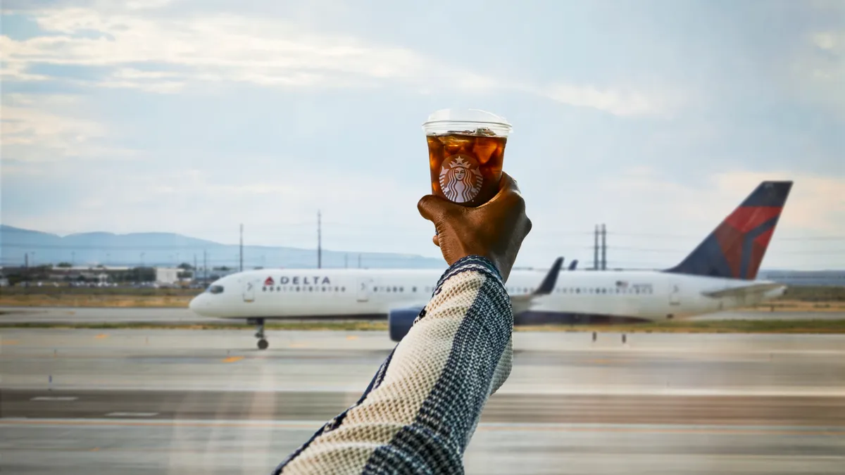 An image showing a hang raising a cup of Starbucks iced coffee with a Delta aircraft in soft-focus in the background.