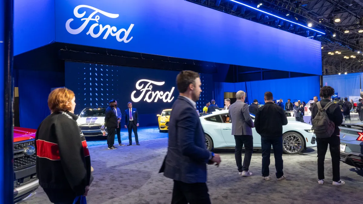 Conference goers walk past the Ford display at a New York auto show