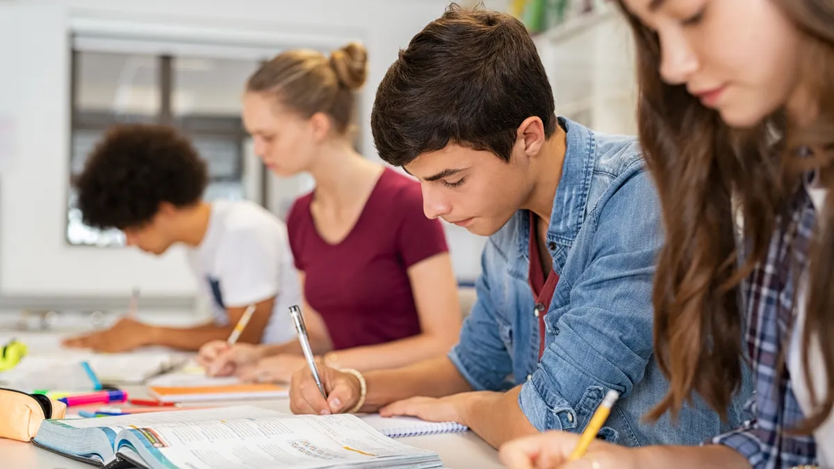 Group of students studying in classroom writing notes during lesson.