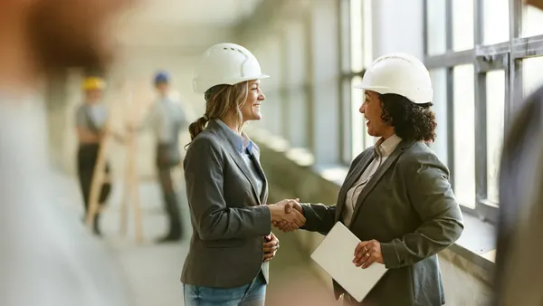 Two women shake hands on a construction site.