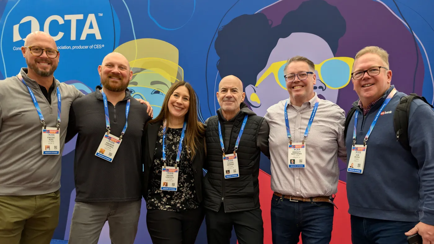 A group of six people poses for a photo in front of a colorful backdrop.