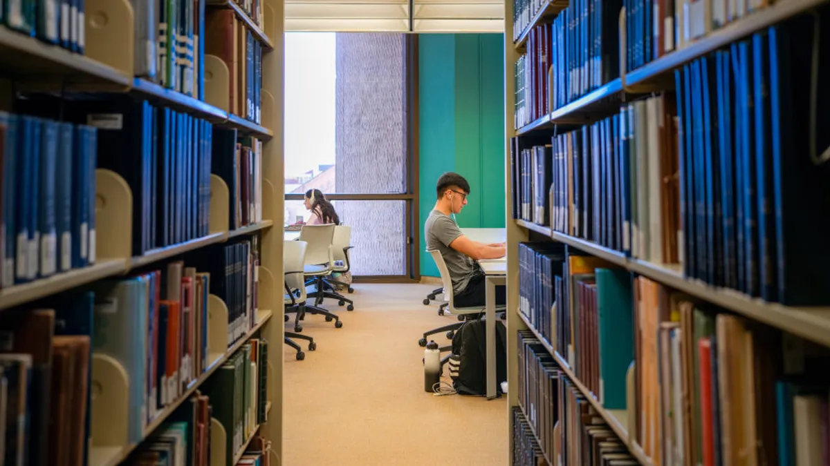 Two students study at separate desks inside a UT-Austin library.