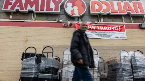 A blurry person in the foreground walks past a "Family Dollar" sign on a yellow brick building.