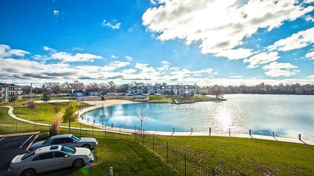 Cars and grass in the foreground with an apartment community in the distance.