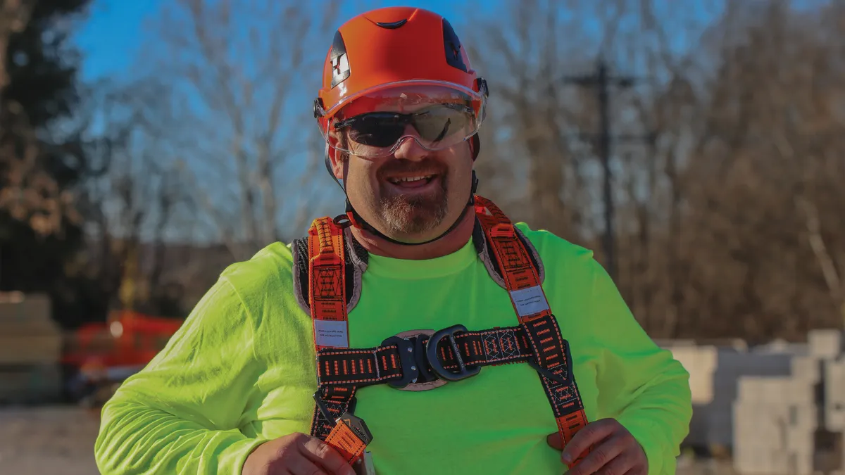 A construction worker with a green shirt and a safety vest with a helmet on