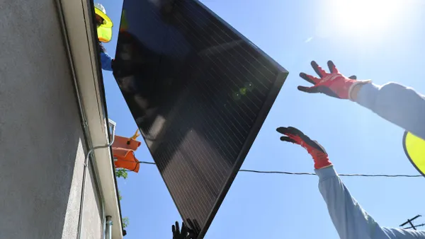 Workers hoist a solar panel on the rooftop of a home