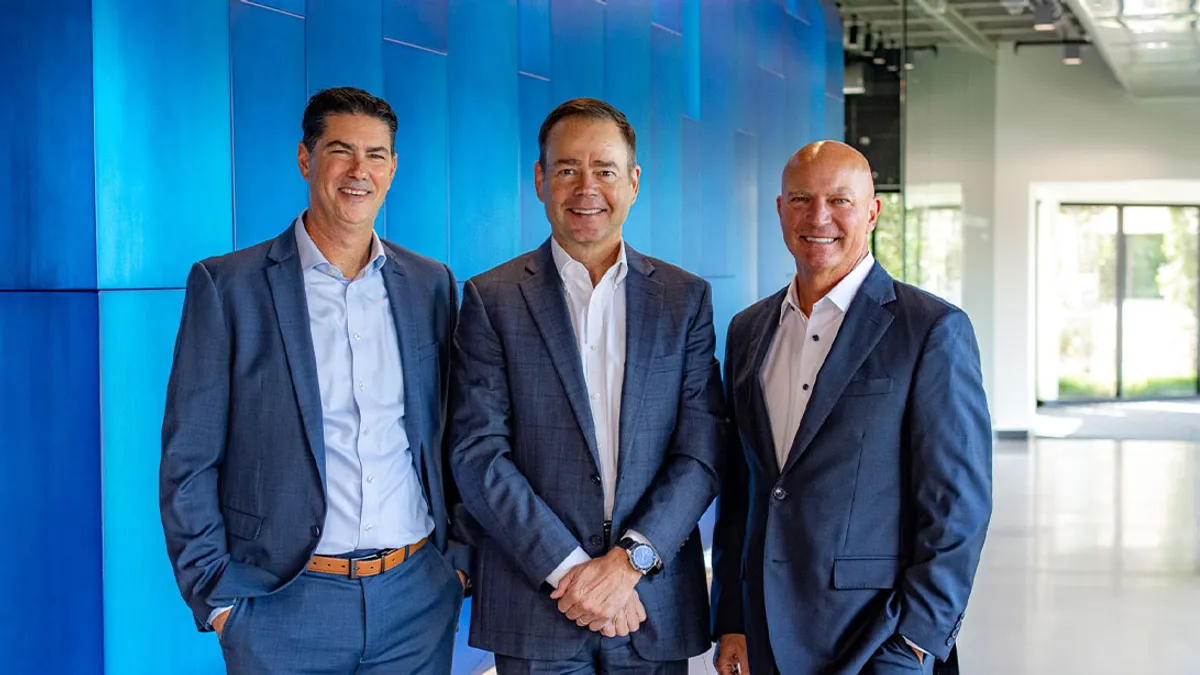 Three men pose for a photograph in professional attire.