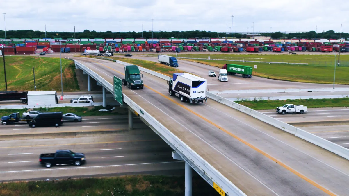 A Gatik truck drives along an overpass as other trucks operate nearby.