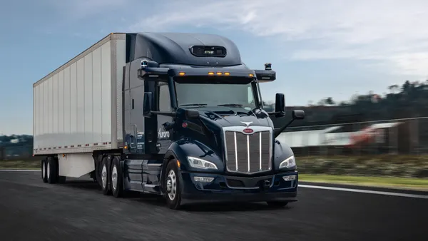An Aurora driverless tractor-trailer on a roadway with a blurry background.
