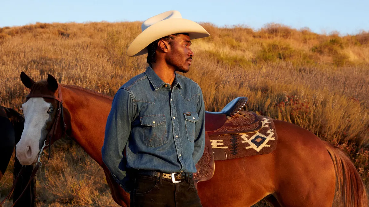 A person wearing a cowboy hat stands in front of a horse.