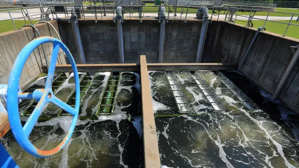 A rusty wheel with blue chipping paint above a concrete basin with flowing water.