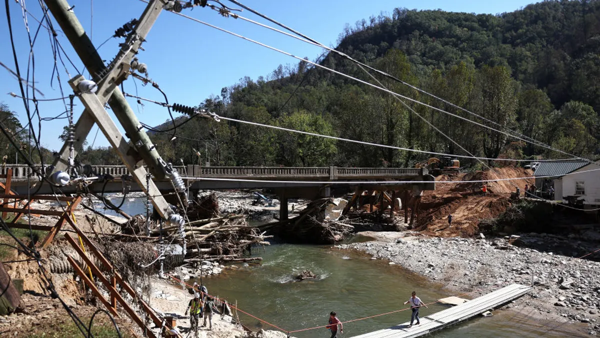 People walk across a makeshift bridge with damaged infrastructure around them.