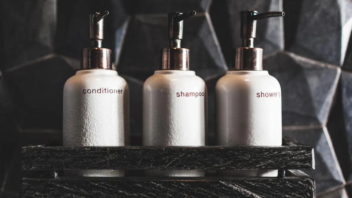 Three white pump bottles in a shower labeled with the words "conditioner," "shampoo" and "shower gel"