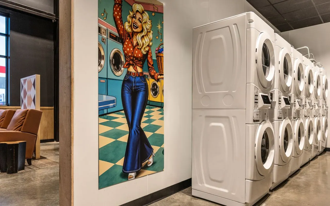 A photo of a trucker's loiunge, showing a bank of washers and dryers, a sitting area and a painting of Dolly Parto0n.