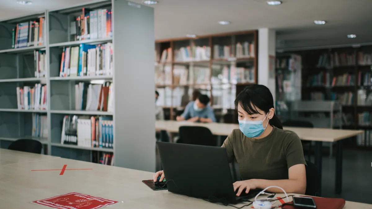 asian university student studying in library observing social distancing